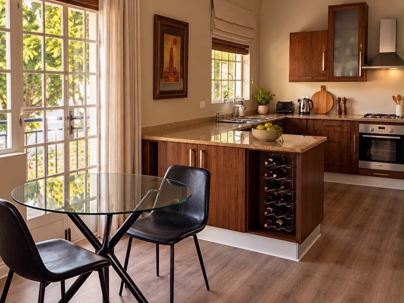 A well-appointed open-plan kitchen and dining area featuring warm wood cabinetry, stone countertops, integrated appliances, and direct access to a balcony through french doors.