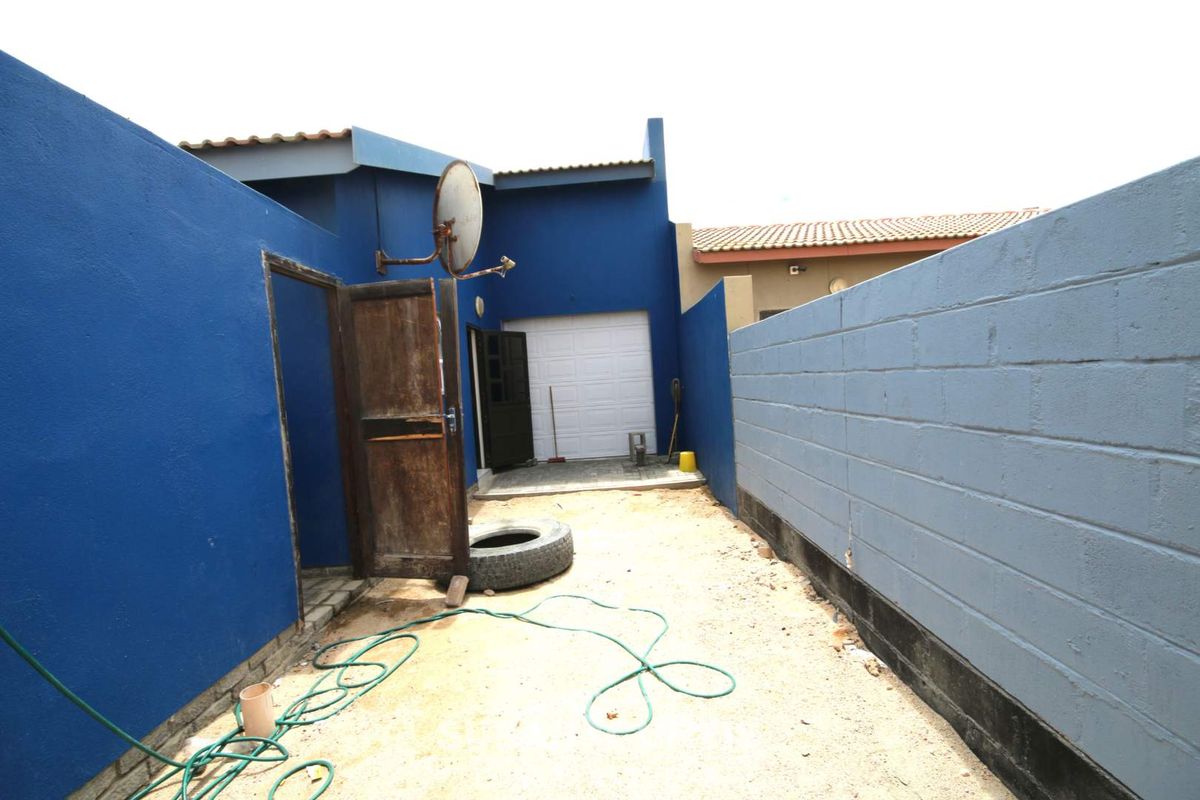 Rear exterior view of the property featuring a blue painted facade, a garage door, and a concrete block boundary wall.