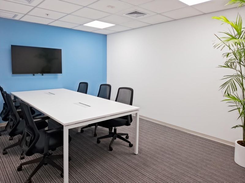 A modern office meeting room featuring a blue accent wall, suspended ceiling with recessed lighting, and neutral carpet flooring.