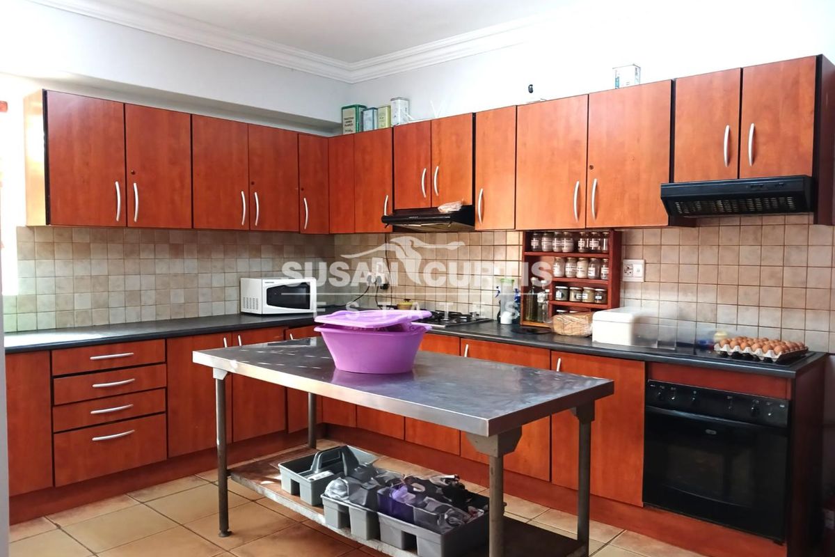 A functional kitchen featuring wood-finish cabinetry, a tiled backsplash, built-in oven, extractor fan, and a stainless steel prep island.