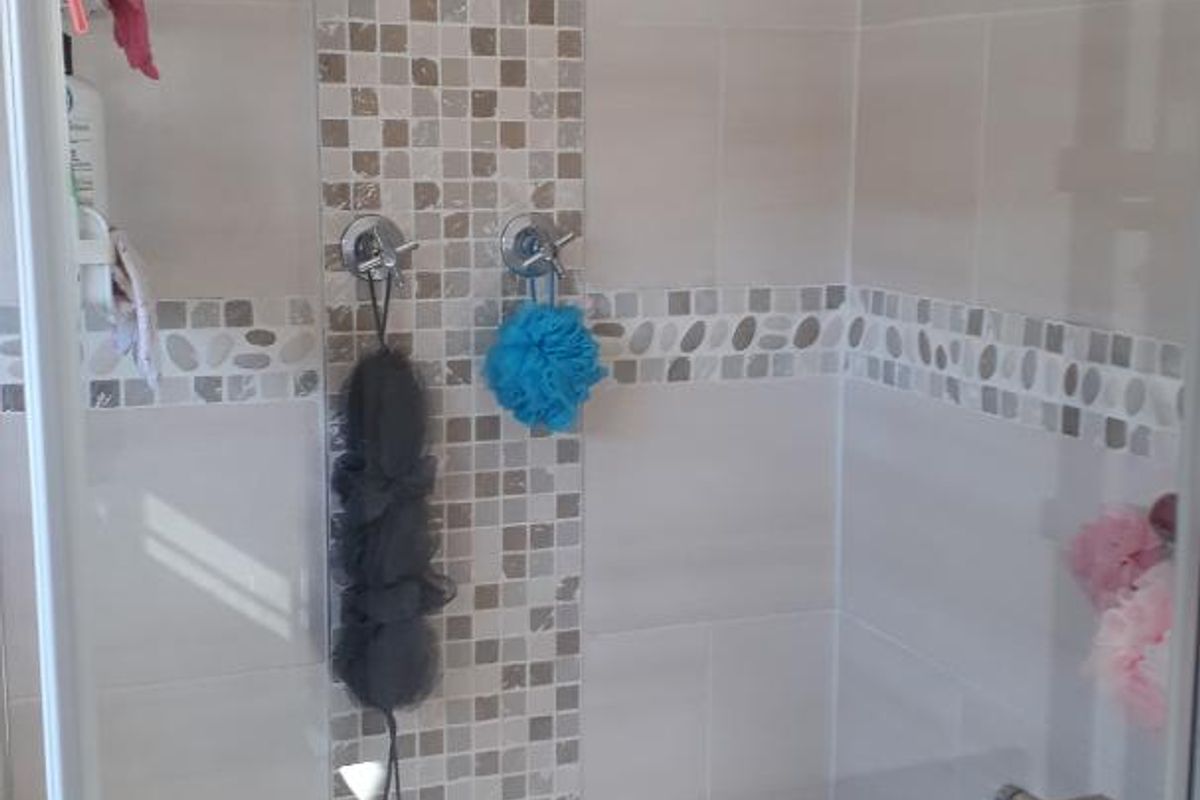 A modern shower enclosure featuring a rainfall shower head, decorative mosaic tile accents, and a glass screen.