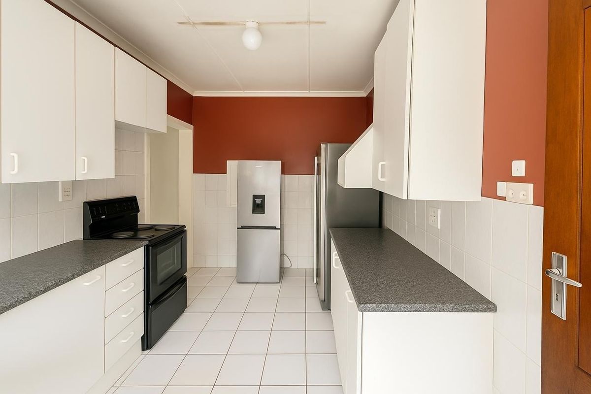 Functional kitchen featuring white cabinetry, dark laminate countertops, tiled splashbacks, and tiled flooring, providing a clean and practical workspace.
