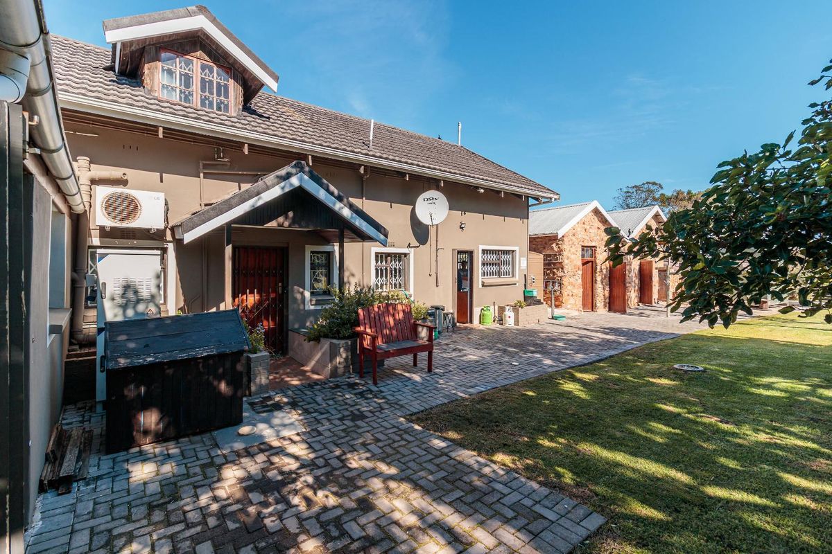 Rear view of the farm property featuring a paved courtyard, established lawn, and multiple building structures with tiled roofing.