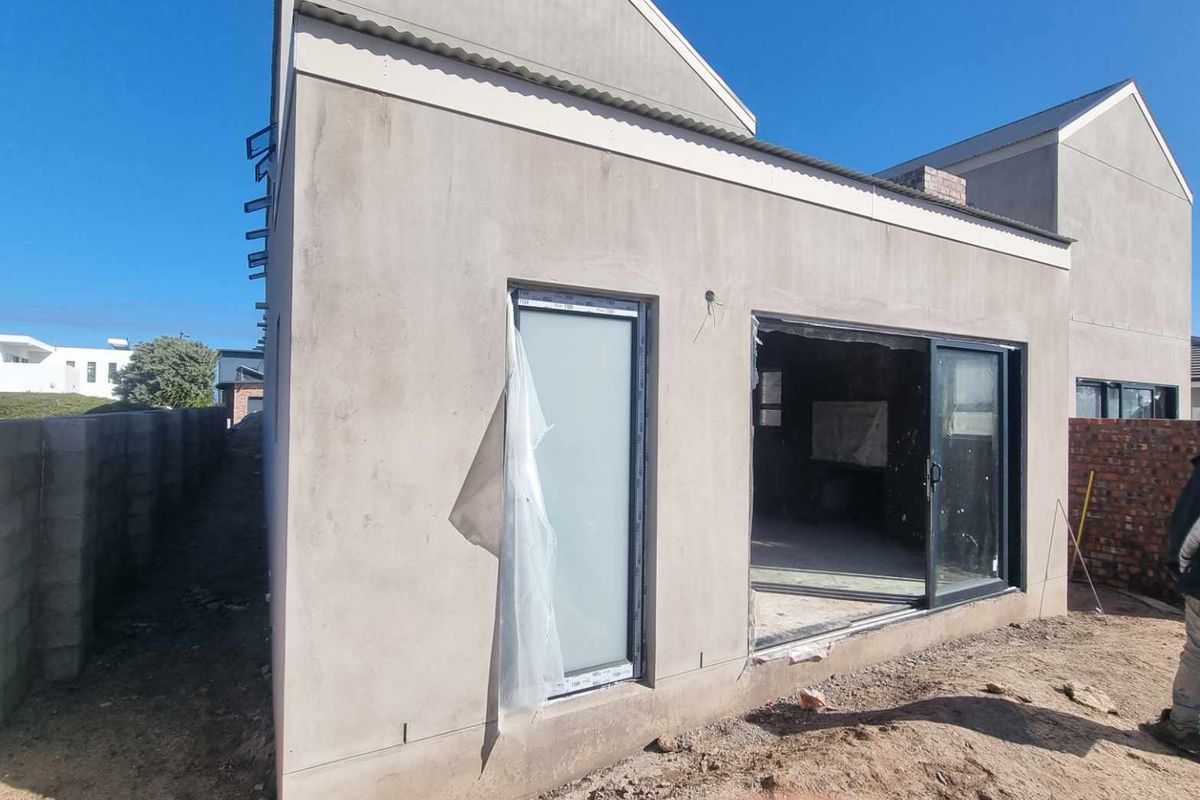 Exterior view of a residential property under construction, featuring modern sliding glass doors and unfinished exterior wall surfaces.