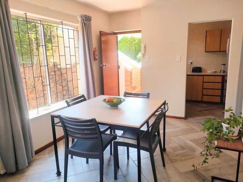 Open plan dining area featuring tiled floors, large window with security bars, and direct access to the kitchen and exterior entrance.
