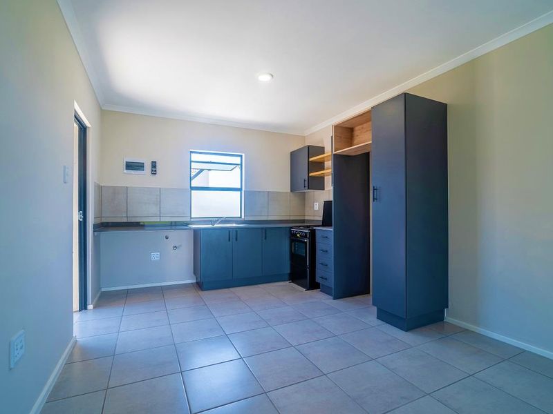 A clean, modern kitchen featuring dark cabinetry, tiled flooring, a stainless steel sink, and a dedicated pantry cupboard in an open-plan layout.