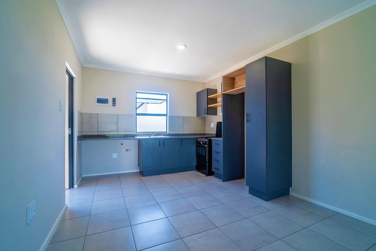 A clean, modern kitchen featuring dark cabinetry, tiled flooring, a stainless steel sink, and a dedicated pantry cupboard in an open-plan layout.
