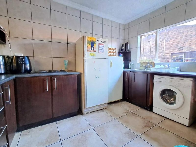 A functional kitchen featuring dark wood cabinetry, tiled walls and floors, a built-in hob, and dedicated plumbing for a washing machine.