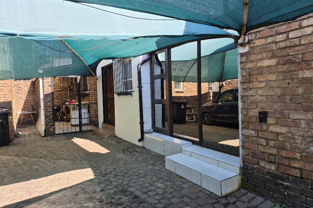 Rear exterior area featuring brick paving, a shade cloth canopy, and a sliding glass door entrance with security features.