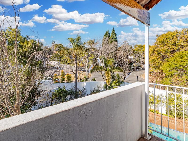 A private balcony featuring timber decking and a metal railing, offering an elevated view of the surrounding neighborhood and garden area.
