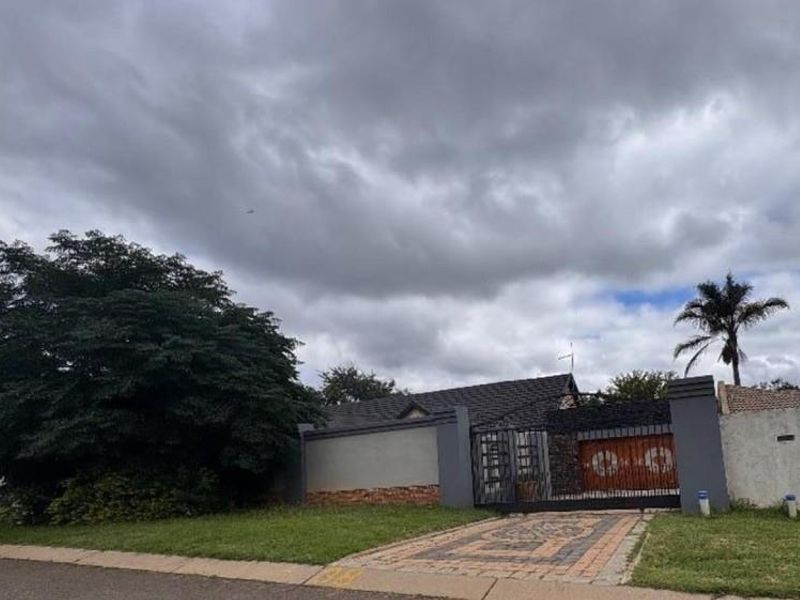 Front view of the property featuring a paved driveway, secure metal gate, and perimeter boundary wall under a cloudy sky.
