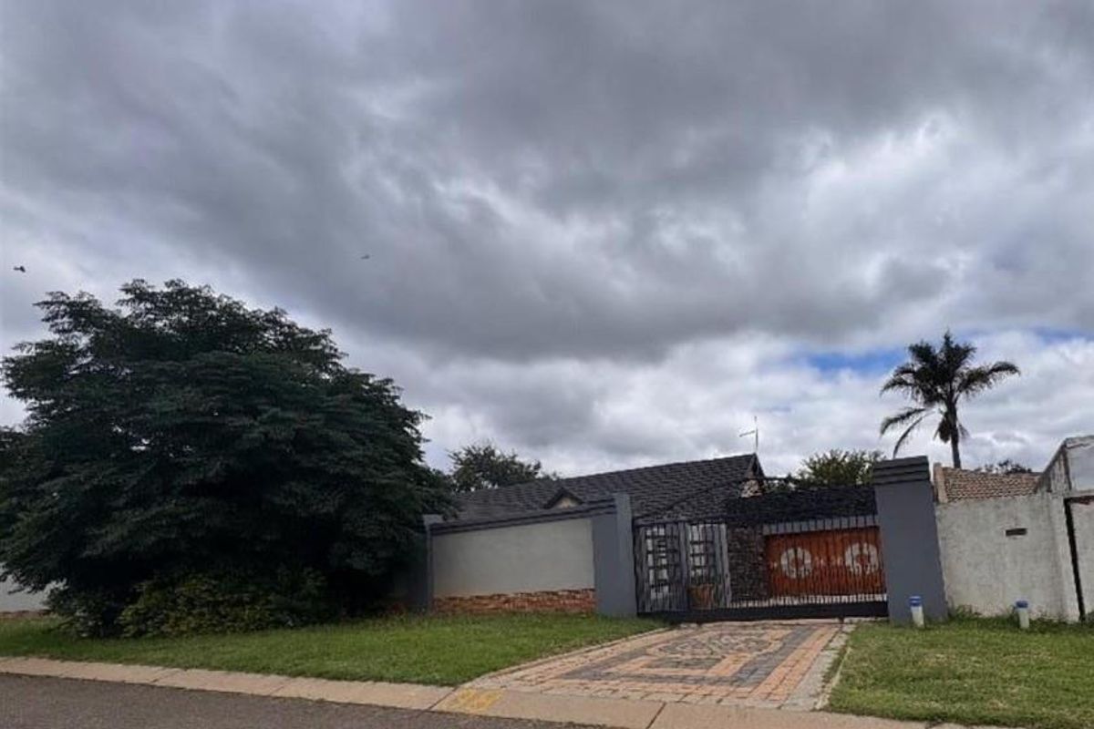 Front view of the property featuring a paved driveway, secure metal gate, and perimeter boundary wall under a cloudy sky.