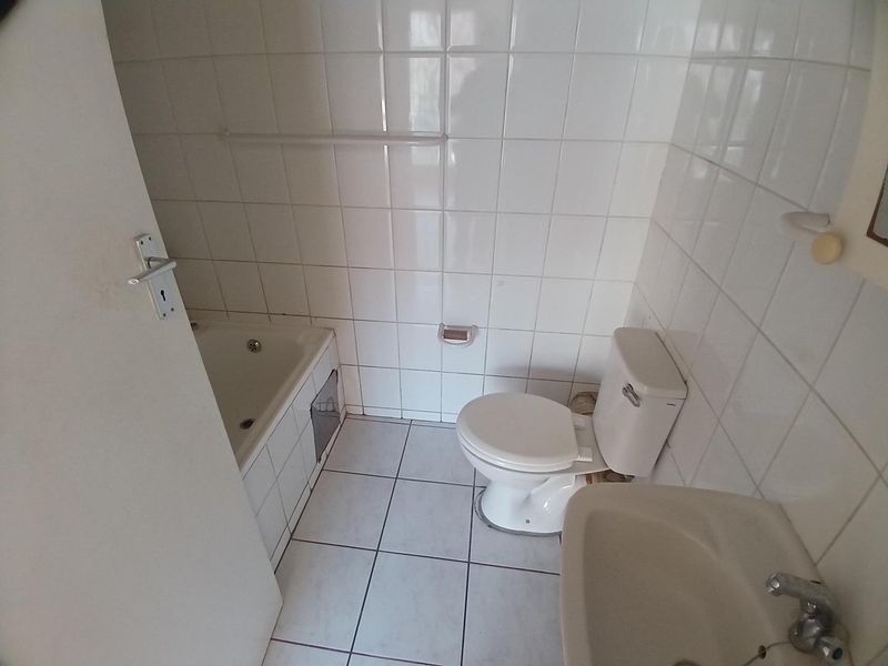 A compact bathroom featuring a built-in bathtub, pedestal basin, and toilet, finished with white ceramic wall and floor tiles.
