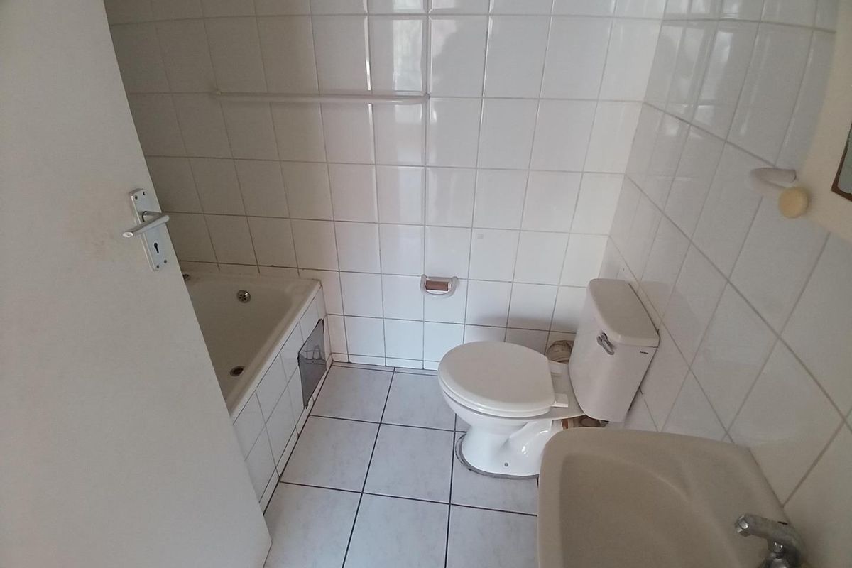 A compact bathroom featuring a built-in bathtub, pedestal basin, and toilet, finished with white ceramic wall and floor tiles.