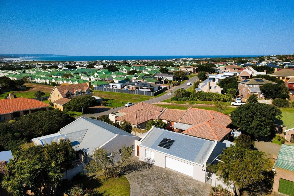Aerial view of the property showing the roof structure, solar panels, paved driveway, and surrounding residential neighborhood with distant ocean views.