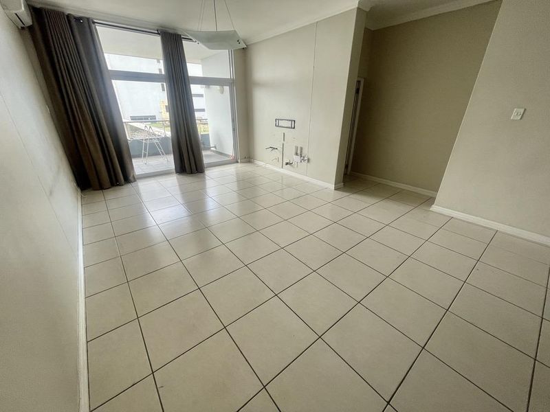 An empty, tiled living room featuring a sliding glass door leading to a balcony and an installed air conditioning unit.