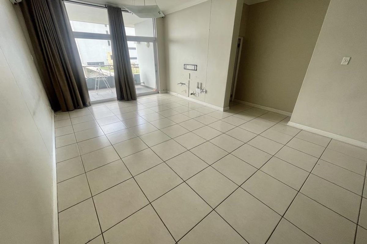 An empty, tiled living room featuring a sliding glass door leading to a balcony and an installed air conditioning unit.