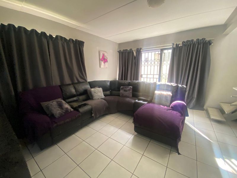 A living room featuring tiled flooring and a sliding door with a security gate, providing access to the exterior.