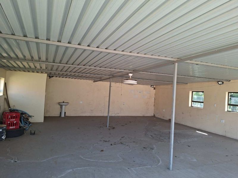 A large, open-plan utility space featuring a corrugated metal roof, concrete flooring, and a built-in pedestal basin, suitable for workshop or storage use.