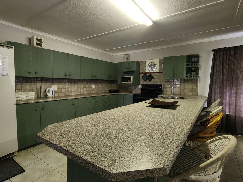 Spacious kitchen featuring extensive green cabinetry, laminate countertops, a large breakfast bar, and tiled backsplash with integrated appliances.