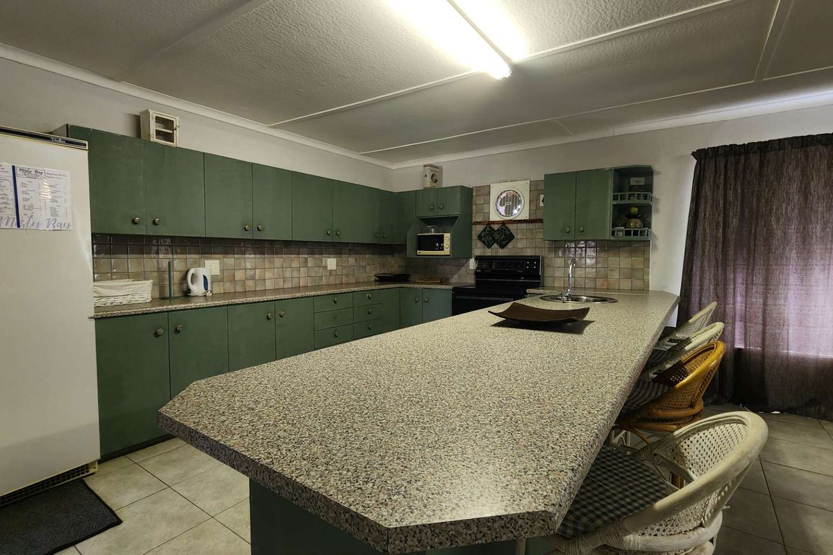Spacious kitchen featuring extensive green cabinetry, laminate countertops, a large breakfast bar, and tiled backsplash with integrated appliances.
