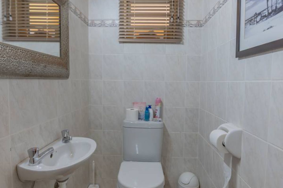 A compact guest bathroom featuring tiled walls, a wall-mounted basin, a standard toilet, and a distinctive timber-paneled ceiling.