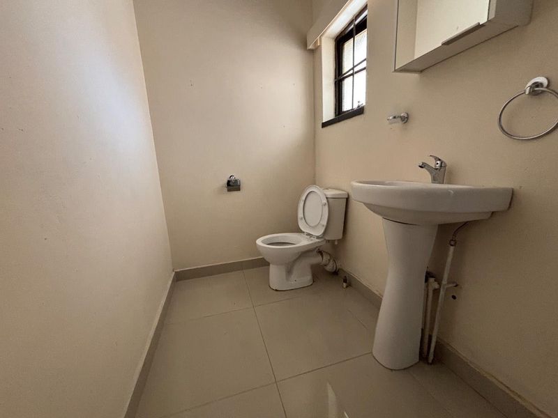 A compact bathroom featuring a pedestal basin, toilet, and tiled flooring, requiring cosmetic updates to improve its overall condition and appeal.