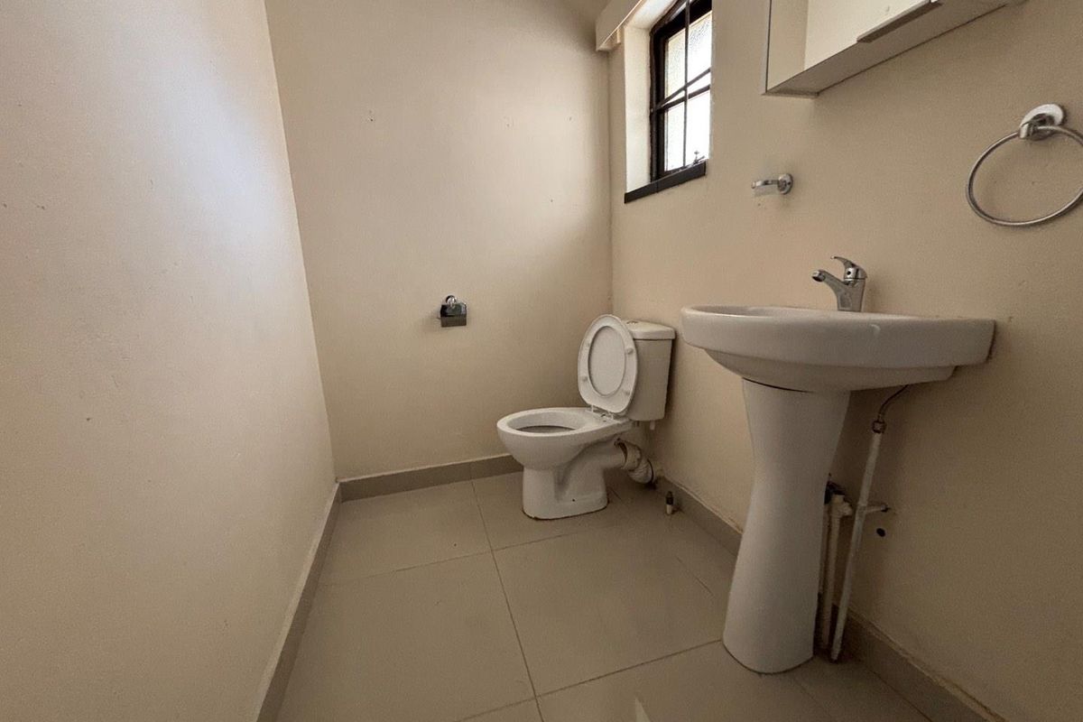 A compact bathroom featuring a pedestal basin, toilet, and tiled flooring, requiring cosmetic updates to improve its overall condition and appeal.