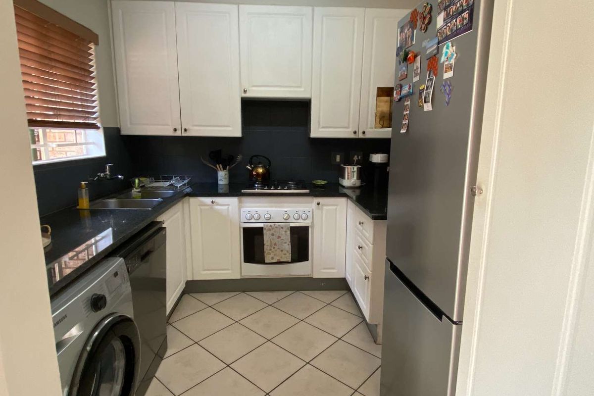Compact kitchen featuring white cabinetry, dark countertops, tiled backsplash, built-in oven, gas hob, and integrated space for laundry appliances.