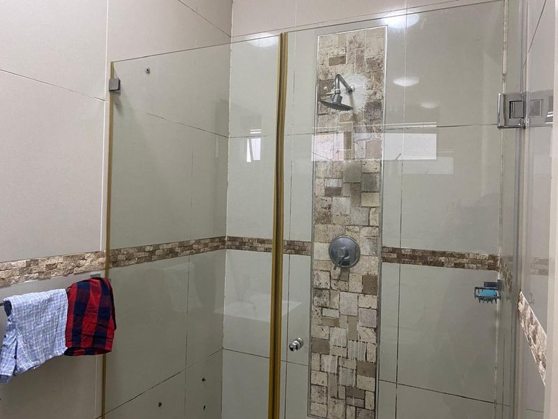 A modern bathroom shower enclosure featuring neutral wall tiles with a decorative mosaic accent strip and a fixed shower head.