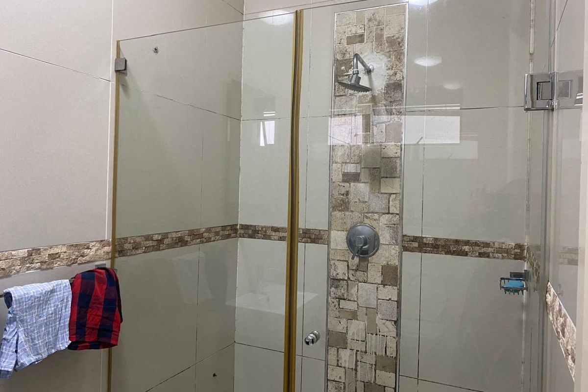 A modern bathroom shower enclosure featuring neutral wall tiles with a decorative mosaic accent strip and a fixed shower head.