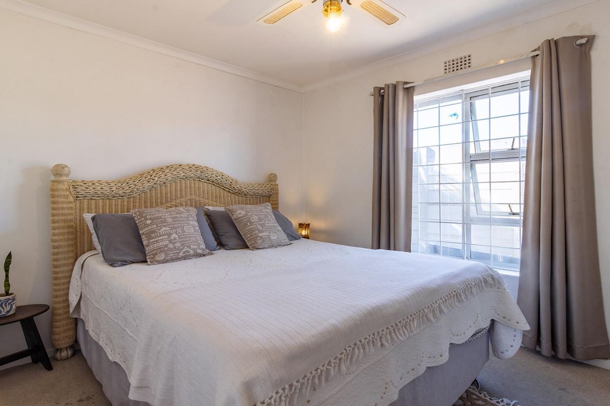 A well-lit bedroom featuring neutral walls, carpeted flooring, a ceiling fan, and a window fitted with security bars.