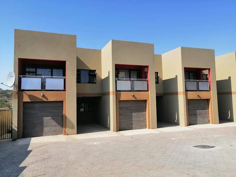 Front elevation of a modern townhouse complex featuring multiple garage units, upper-level balconies with metal railings, and a paved driveway area.
