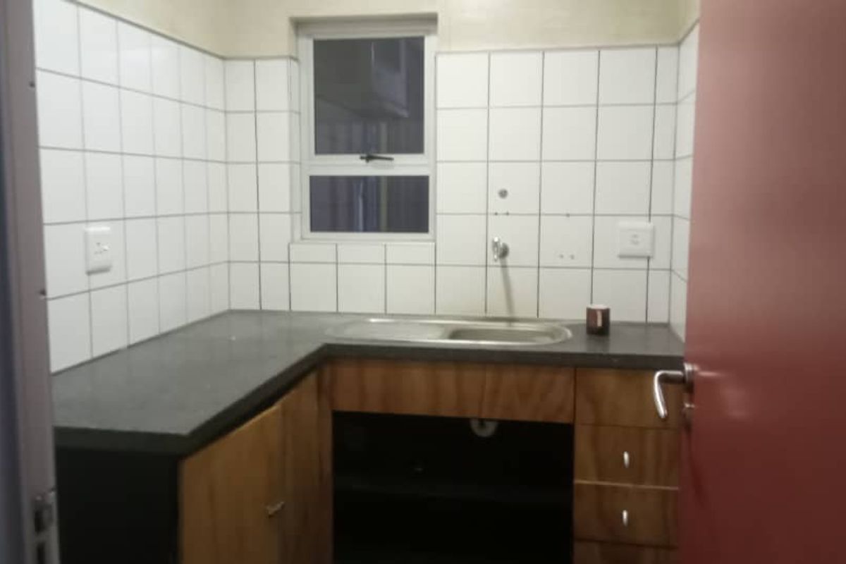 A functional kitchenette featuring a stainless steel sink, laminate countertops, and wood-finish cabinetry with tiled splashbacks.