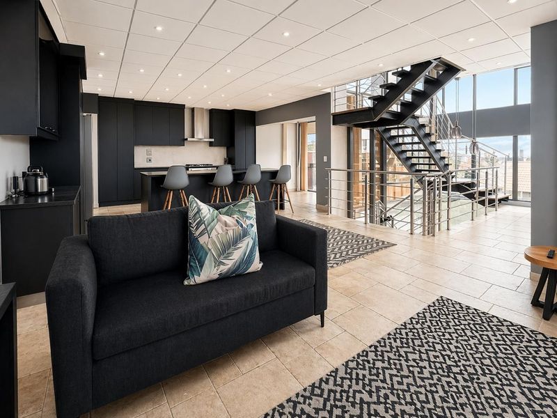Modern open-plan living area featuring a sleek black kitchen, central island, and a striking industrial-style staircase with metal railings.