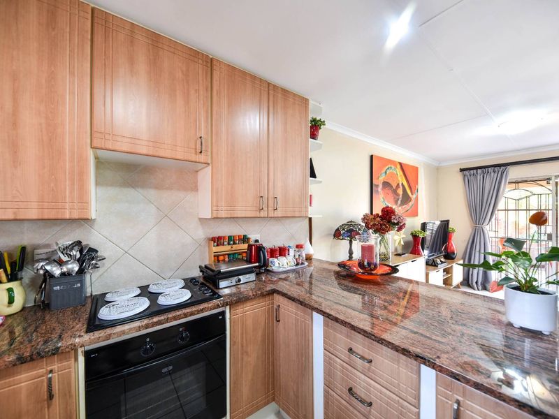 Open-plan kitchen featuring wood-finish cabinetry, granite countertops, and integrated appliances, flowing into a living area with access to an outdoor space.