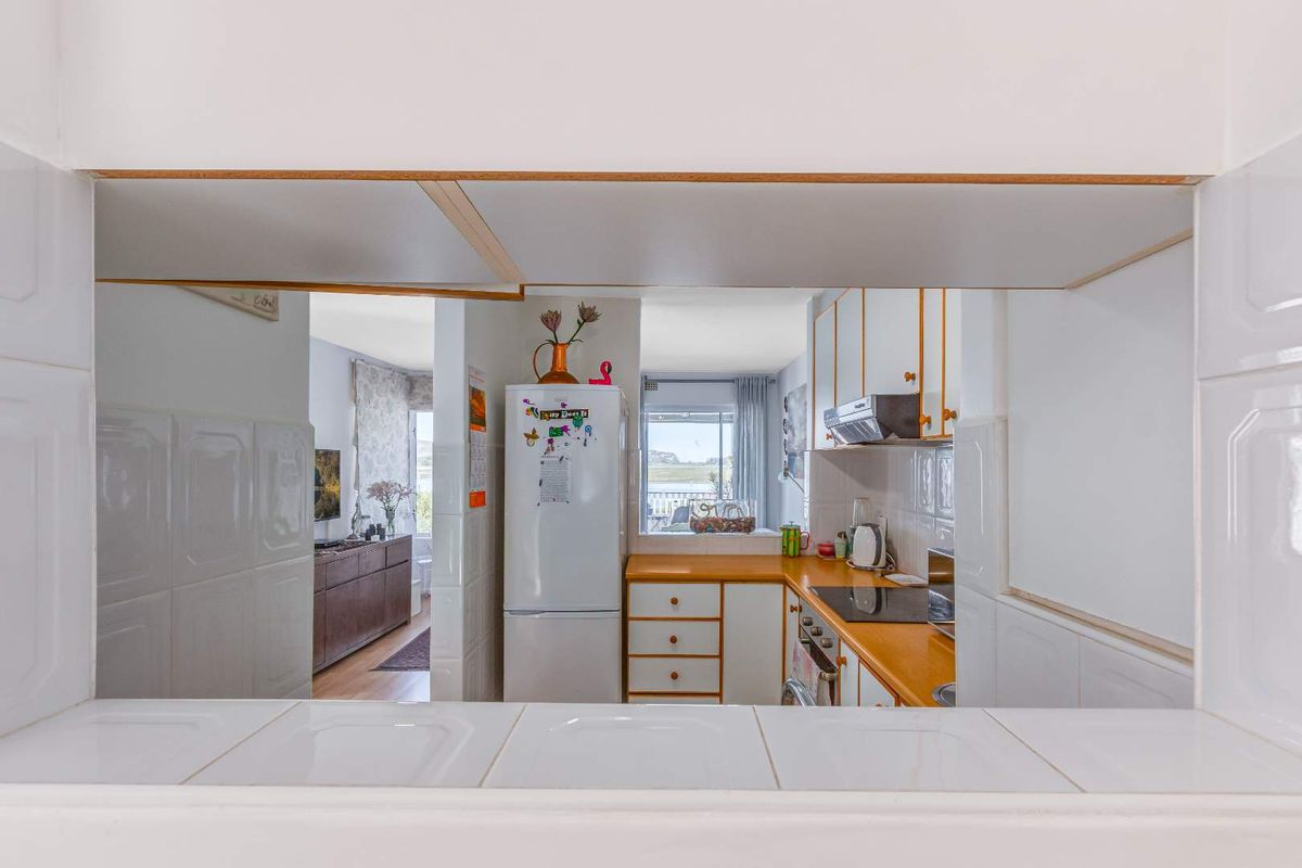 A functional kitchen featuring built-in cabinetry, a cooktop, and an extractor fan, with a convenient serving hatch opening into the adjacent living area.