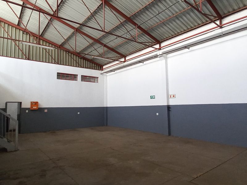 Spacious industrial warehouse unit featuring high-clearance exposed steel truss roofing, concrete flooring, and dual-tone painted walls with integrated fire safety signage.