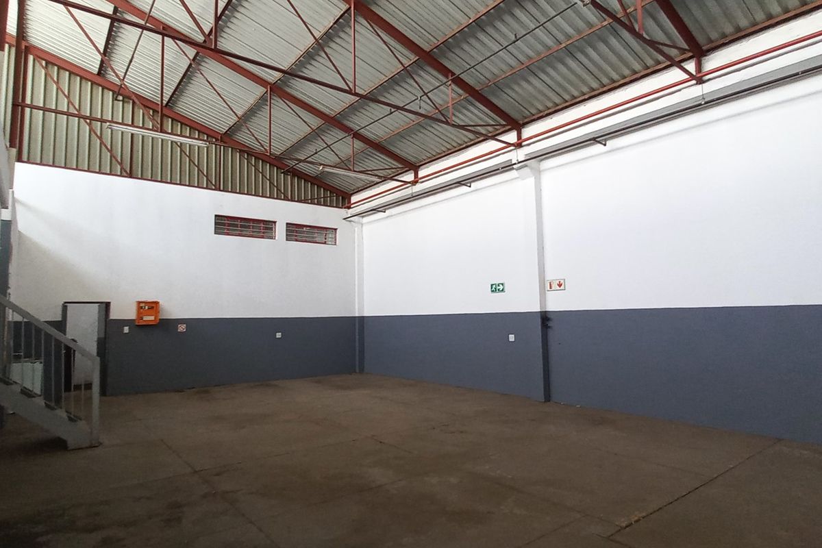 Spacious industrial warehouse unit featuring high-clearance exposed steel truss roofing, concrete flooring, and dual-tone painted walls with integrated fire safety signage.
