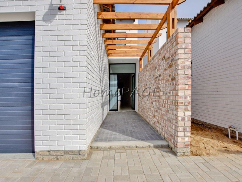 Modern townhouse entrance featuring a timber pergola, exposed brick wall, and paved walkway leading to a glass front door.
