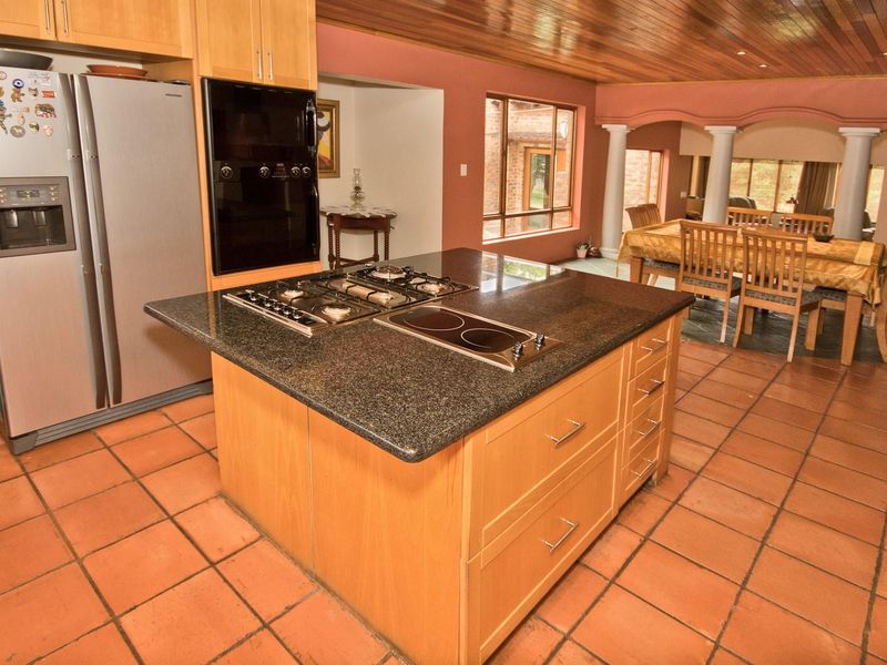 Open plan kitchen and dining area featuring a central island with dual hobs, granite countertops, timber ceilings, and terracotta floor tiles.