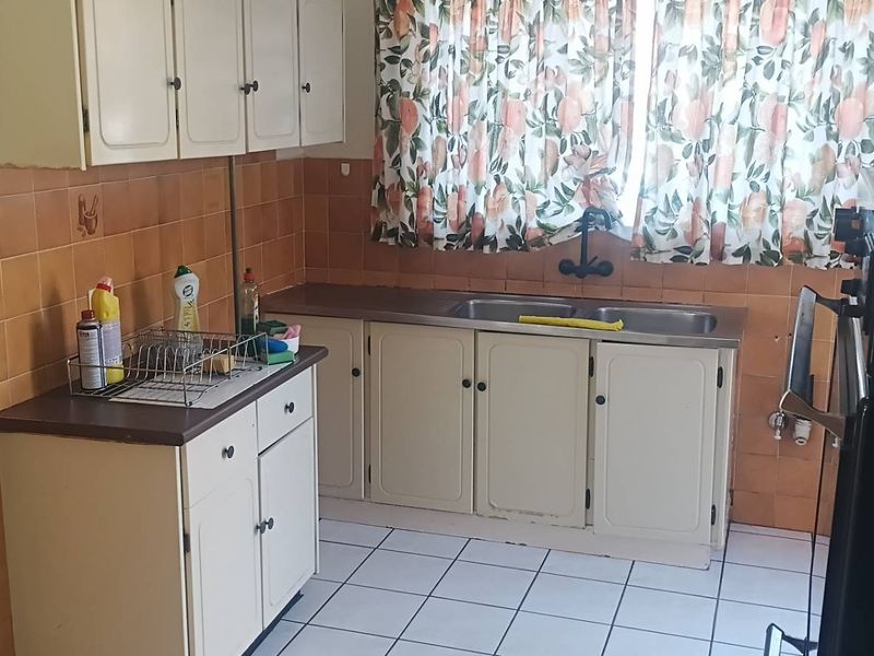 A dated kitchen featuring original cabinetry, tiled splashbacks, a double basin sink, and built-in oven, offering significant potential for modernization.
