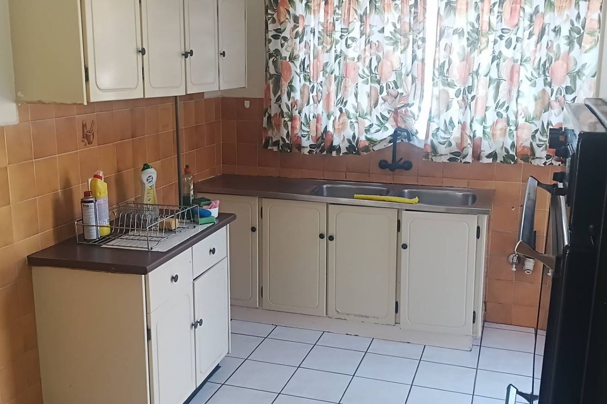 A dated kitchen featuring original cabinetry, tiled splashbacks, a double basin sink, and built-in oven, offering significant potential for modernization.