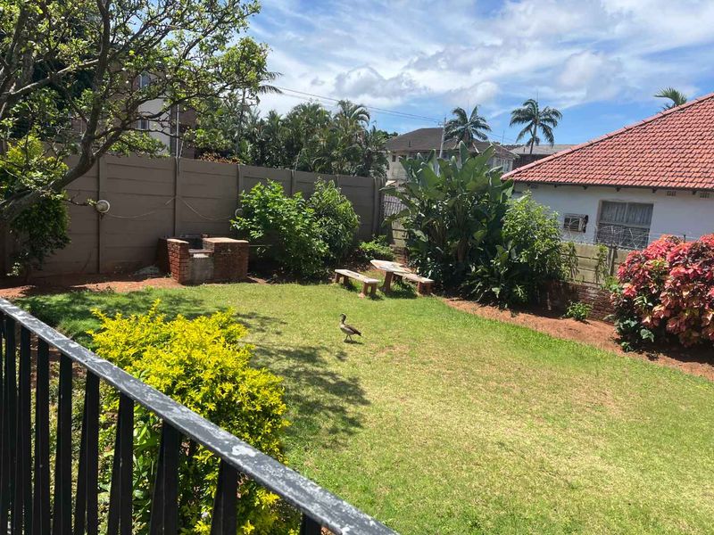 A private rear garden featuring a lawn, established landscaping, a brick braai area, and a secure boundary wall.