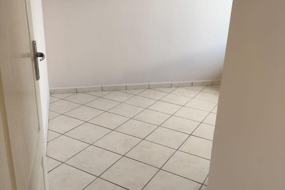 An empty bedroom featuring neutral tiled flooring and plain walls, offering a blank canvas for personalization.
