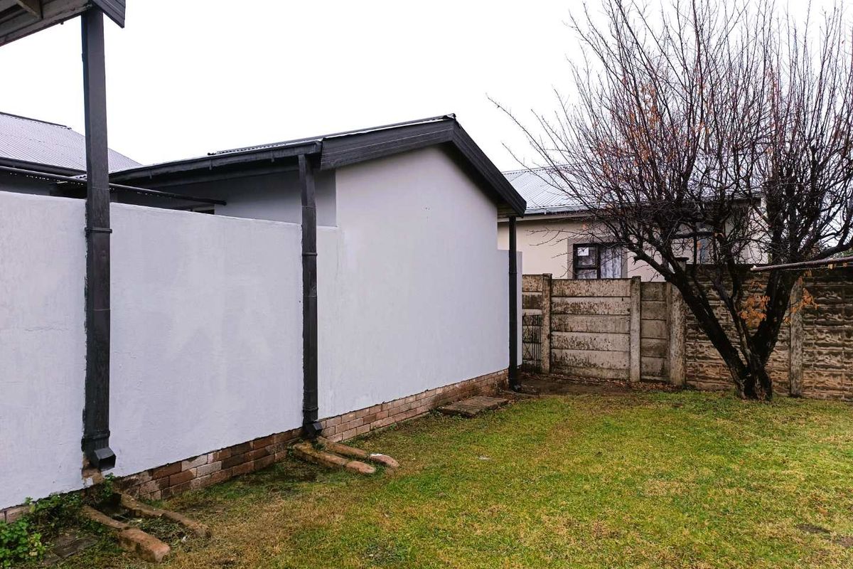 A view of the rear exterior of the property, featuring a painted wall, guttering system, and a small garden area with a boundary wall.