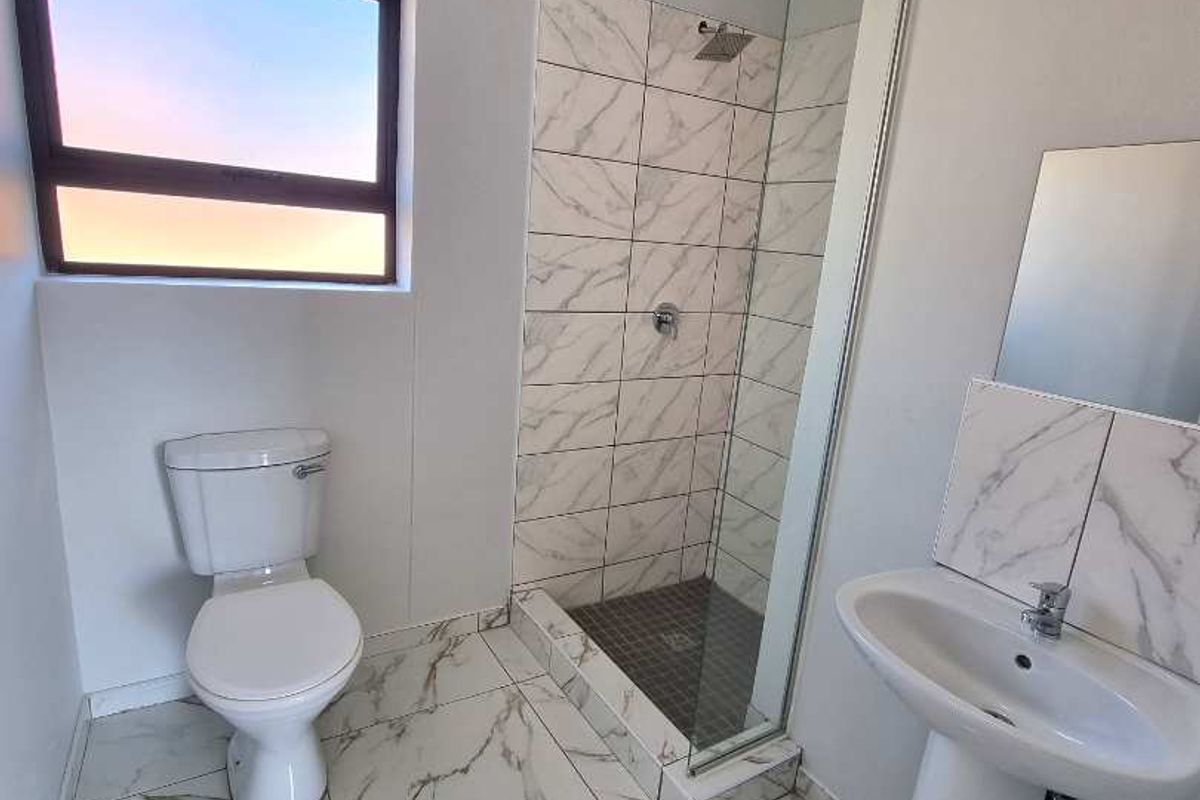 Modern bathroom featuring a glass-enclosed shower, pedestal basin, and toilet with marble-look floor and wall tiling.