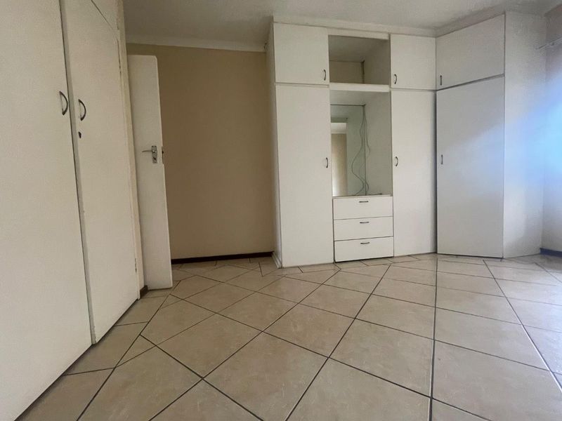 A vacant bedroom featuring neutral tiled flooring and extensive white built-in cupboards with an integrated vanity mirror.