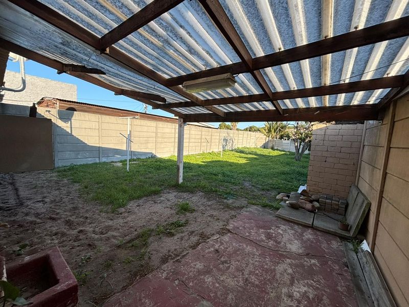 Covered outdoor patio area featuring a timber pergola structure and concrete flooring, overlooking a spacious backyard enclosed by precast concrete walls.