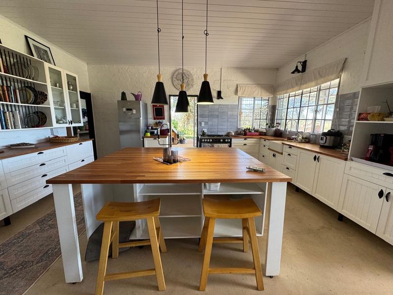 A bright, farmhouse-style kitchen featuring white cabinetry, butcher block countertops, a classic farmhouse sink, and a central island with pendant lighting.